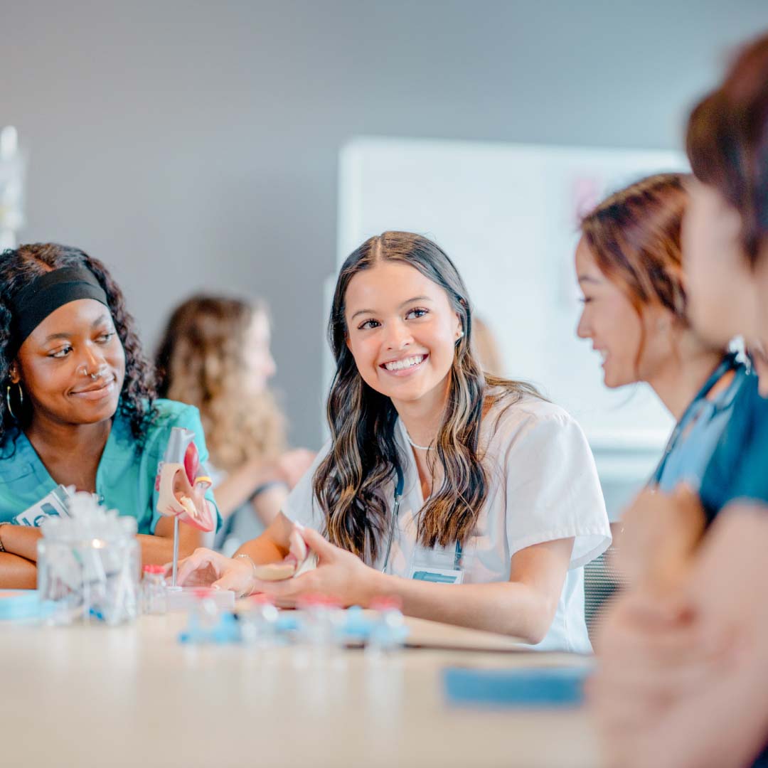 A group of nursing students sitting around a desk practicing their clinical skills.