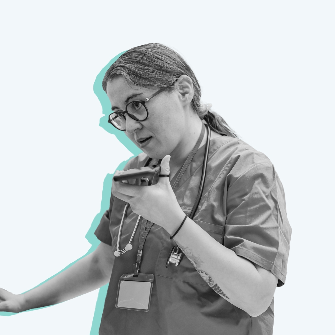 A nurse using a computer and speaking into a smartphone. 